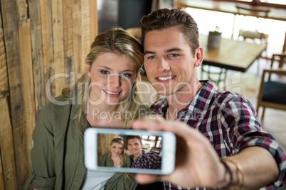 Smiling couple taking selfie with mobile phone in cafeteria