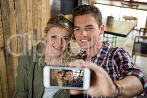 Smiling couple taking selfie with mobile phone in cafeteria