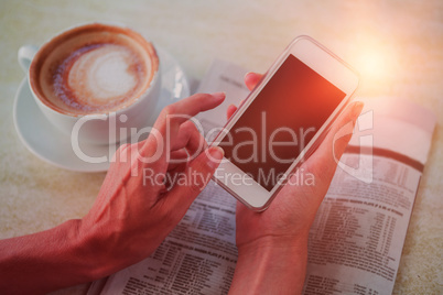 Man using mobile phone by coffee and newspaper in cafe