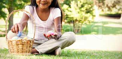 Little girl sitting on grass counting easter eggs smiling at camera