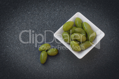 Green olives in a white bowl on a black surface