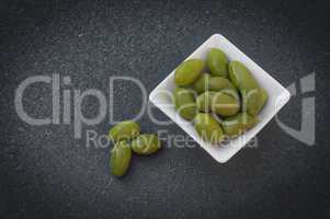 Green olives in a white bowl on a black surface