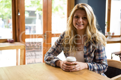 Smiling young woman holding disposable coffee cup in cafe