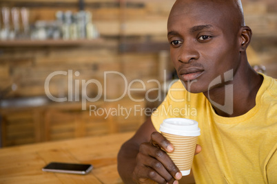 Thoughtful man holding disposable coffee cup in cafe