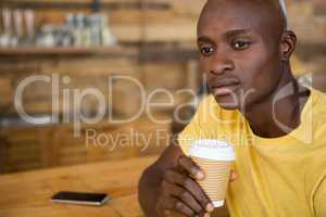 Thoughtful man holding disposable coffee cup in cafe