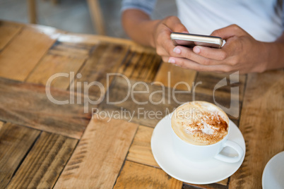 Woman using mobile phone with coffee cup on table at cafe