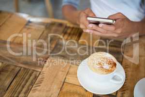 Woman using mobile phone with coffee cup on table at cafe