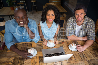 Happy friends having coffee with laptop on wooden table in cafe
