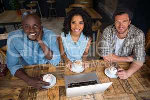 Happy friends having coffee with laptop on wooden table in cafe