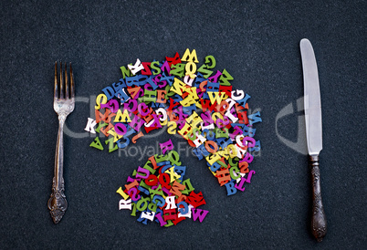 Cutlery and multicolored letters of wood on a black surface