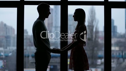Silhouette of couple holding hands by window