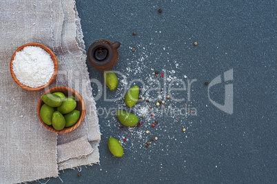 Olives and salt in wooden bowls, black surface