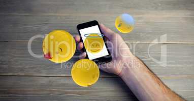 Close-up of hands holding smart phone with various emojis at wooden table