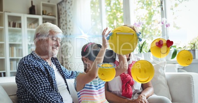 Grandfather looking at granddaughter touching emojis seen through VR glasses