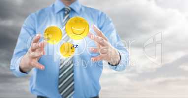Business man mid section with flares and emojis between hands against cloudy sky