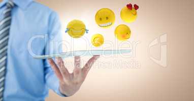 Business man mid section holding tablet with one hand and emojis against cream background