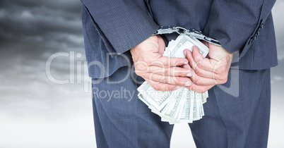 Close up of business man's hands behind back with money and handcuffs against white wall