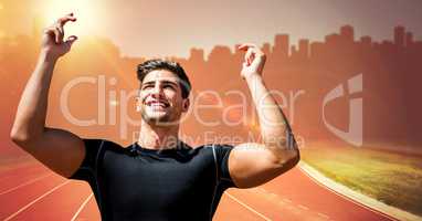 Male runner with hands in air on track against orange flare and blurry skyline