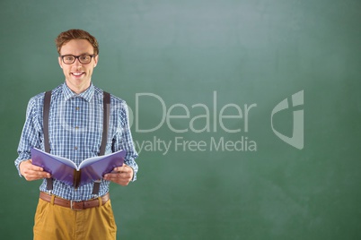 Happy male college student holding book while standing against chalkboard