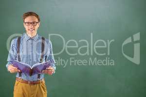 Happy male college student holding book while standing against chalkboard