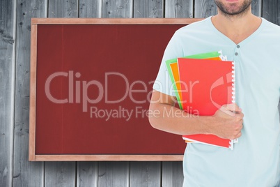 Midsection of male college student holding books while standing against notice board