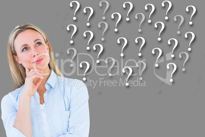 Thoughtful businesswoman looking at question marks against gray background