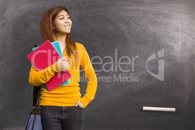 Female student holding books against blackboard