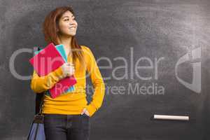 Female student holding books against blackboard
