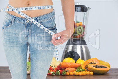 Midsection of woman measuring waist with juicer and fruits in background