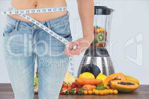 Midsection of woman measuring waist with juicer and fruits in background