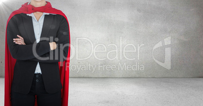 Business woman superhero with arms folded against grey wall with flare