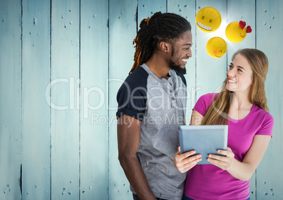 Man and woman with tablet and emojis against blue wood panel