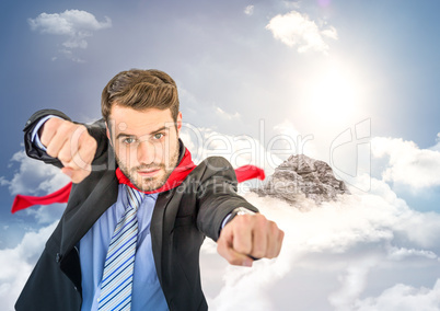 Business man superhero with hands out against mountain peak with clouds