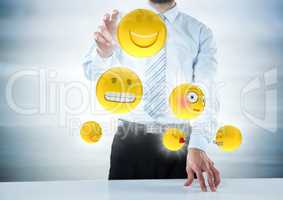 Business man with hand on desk and emojis with flares against blurry grey wood panel;