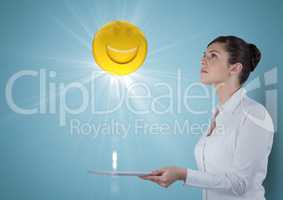 Business woman with tablet looking up at emoji and flare against blue background