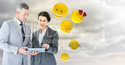 Business people with tablet against cloudy sky with emojis
