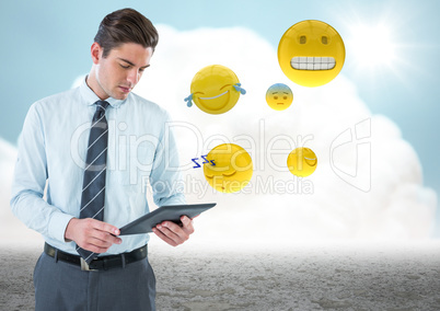 Business man with tablet and emojis against cloud and ground