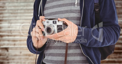 Man with camera mid section against blurry wood panel