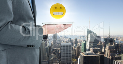 Business man mid section with tablet and emoji with flare against skyline