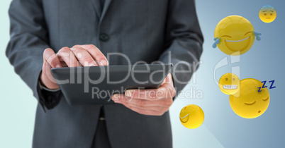 Business man mid section with tablet next to emojis and flare against blue background