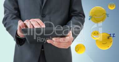 Business man mid section with tablet next to emojis and flare against blue background