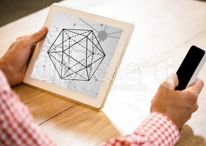 Hands at desk holding phone and tablet showing hexagon against grey interface