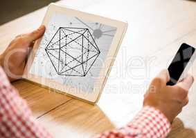 Hands at desk holding phone and tablet showing hexagon against grey interface