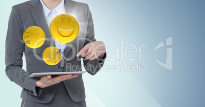 Business woman mid section with tablet and emojis with flare against blue background