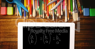 Overhead view of formula in digital tablet with color pencils and school supplies on wooden table