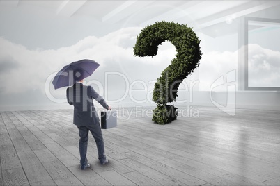 Businessman with umbrella and briefcase looking at question mark made of plants