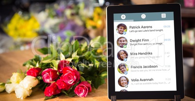 Close-up of chat list on digital tablet by flower at table