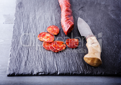 Spanish chorizo with a knife on a stone plate.