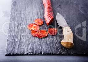 Spanish chorizo with a knife on a stone plate.