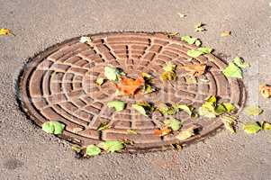 Manhole under a colorful dry autumn leaves